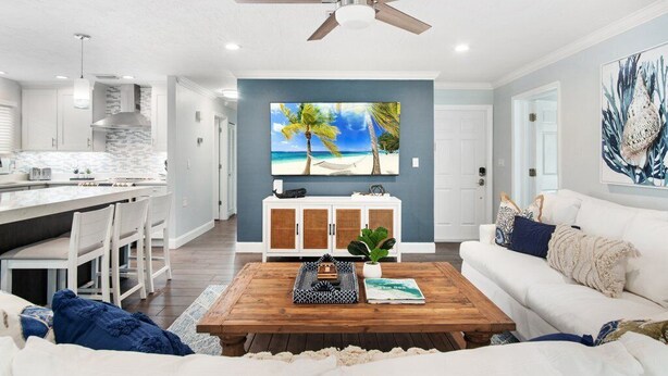 A modern living room with a wooden coffee table, white sofa, and a large painting of a beach scene. - Coastal Retreat w/ Porch, Games, Pet Friendly! (Naples)