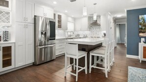 A modern kitchen with white cabinetry, stainless steel appliances, and a central island with bar stools. - Coastal Retreat w/ Porch, Games, Pet Friendly! (Naples)