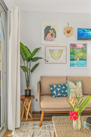 Een woonkamer met een bank, een bijzettafeltje, een potplant en wanddecoratie.