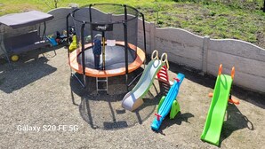 Un parque infantil con un trampolín, tobogán y columpios.