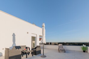 A rooftop terrace with outdoor furniture, a white umbrella, and a view of the landscape.