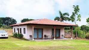 A single-story building with a red-tiled roof, a covered porch with chairs, and a car parked in front. - 2 bdrm Villa, walk to square (pedasi)