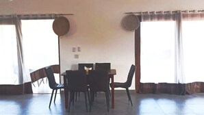 A dining area with a table and chairs, large windows with curtains, and a flat-screen TV on the wall. - 2 bdrm Villa, walk to square (pedasi)