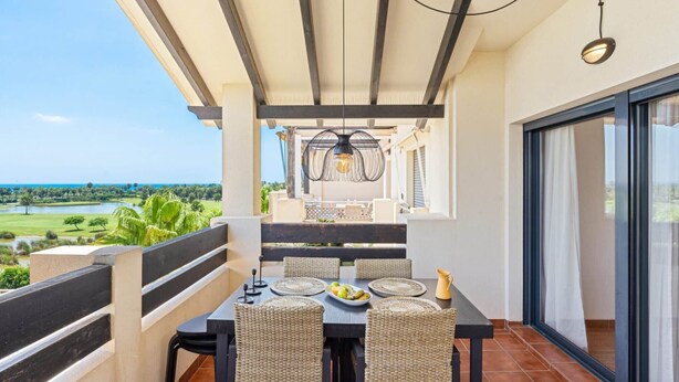 Een balkon met een eettafel, rieten stoelen, een hanglamp en uitzicht op een golfbaan.