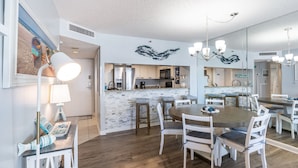 A modern kitchen with a stone backsplash, white cabinetry, and a central island. There are bar stools and a dining table with chairs. - S Hampton 1403 1 Br Oceanview in Kingston, Pool (Myrtle Beach)