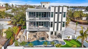 A modern multi-story house with a swimming pool, a waterfall feature, and a balcony with outdoor seating. - Pirate House: Gulf Front, Pool, #1 Location Lido Key, St. Armands One Block. (Sarasota)