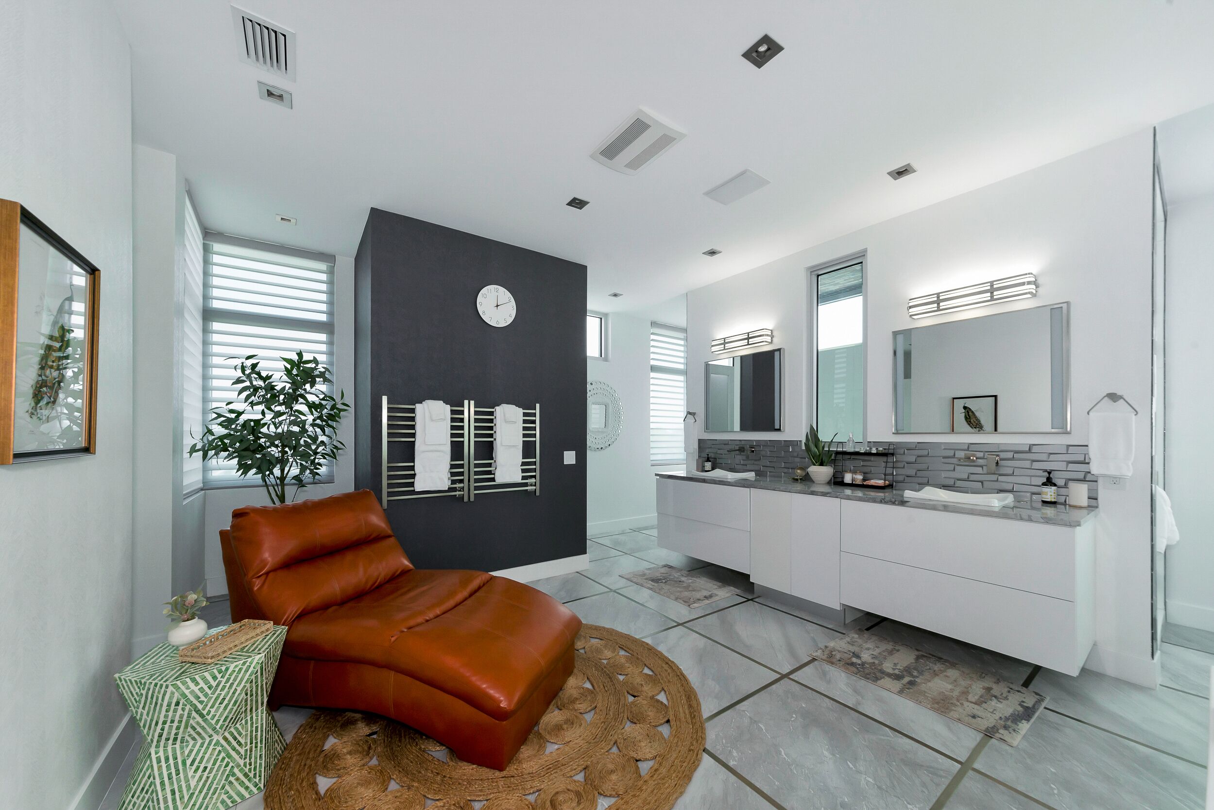 Une salle de bain moderne avec un grand miroir, des meubles blancs et un tapis rond.