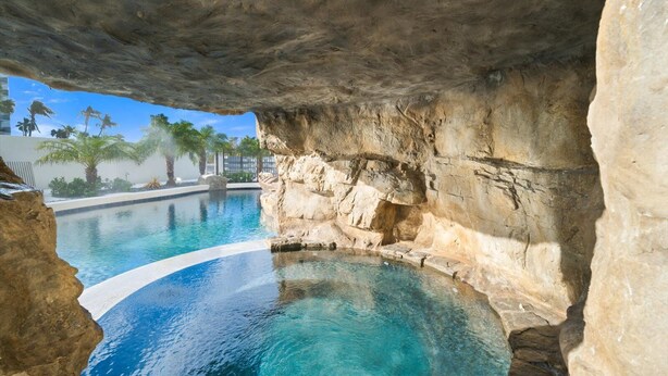 A swimming pool with clear blue water, surrounded by natural rock formations and palm trees. - Pirate House: Gulf Front, Pool, #1 Location Lido Key, St. Armands One Block. (Sarasota)