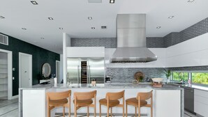 A modern kitchen with a central island, bar stools, a stainless steel range hood, and a view of greenery outside. - Pirate House: Gulf Front, Pool, #1 Location Lido Key, St. Armands One Block. (Sarasota)