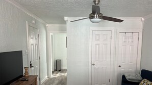 Un dormitorio con ventilador de techo, un televisor sobre un aparador de madera, un sofá azul oscuro y una puerta blanca.