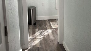 Un pasillo con un bote de basura, una alfombra y dos cuadros en la pared.