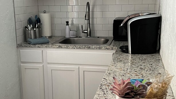 Una cocina con armarios blancos, encimera de granito, pileta de acero inoxidable y cafetera.