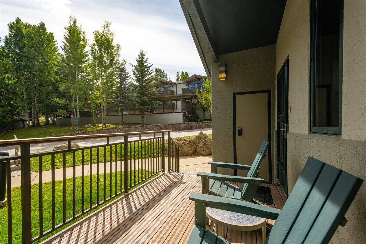 A balcony with wooden flooring, a metal railing, and two green chairs.