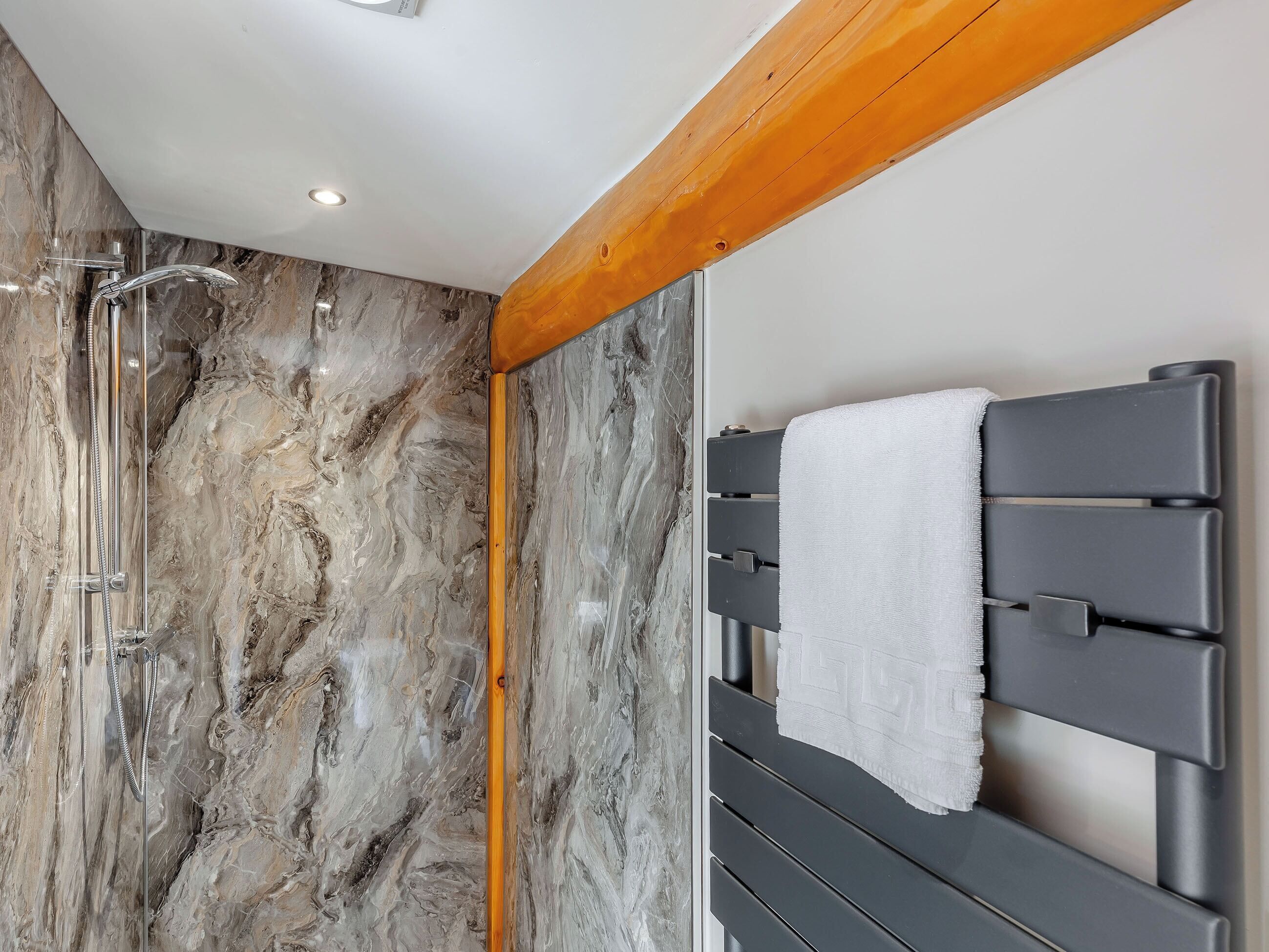 Een badkamer met een douche, marmeren wanden en een handdoekrek.