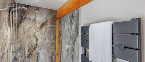 Een badkamer met een douche, marmeren wanden en een handdoekrek.