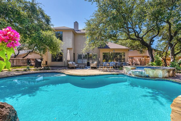 Une piscine avec un espace patio, entourée d’arbres et d’une maison.