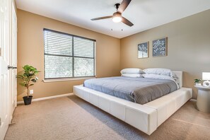 Une chambre à coucher avec un lit, un ventilateur de plafond, une fenêtre, une plante en pot et des œuvres d’art murales.