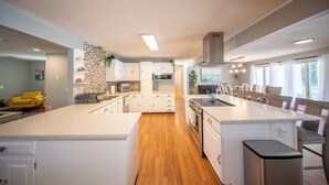 Een moderne keuken met witte kasten, een centraal eiland en een eethoek met stoelen.
