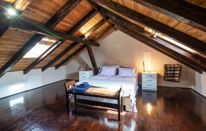 Cozy attic retreat with a single bed, bedside table, and chair, set beneath a sloping ceiling with a skylight.