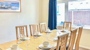 Une table à manger dressée pour six personnes, avec de l’assiette blanche, des bols et des verres à vin, entourée de chaises en bois.