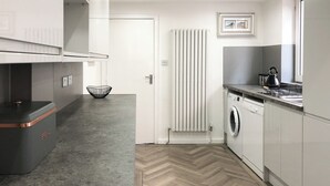 Une cuisine moderne dotée d’un four encastré, d’un lave-linge et d’un plancher à motifs en chevrons.