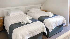 Une chambre double avec deux lits, chacun étant équipé d’un oreiller, d’une table de chevet et d’une serviette pliée posée sur le lit.