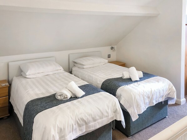 A twin room with two beds, each with a pillow, a nightstand, and a folded towel on the bed. - 4 bedroom accommodation in Keswick (Keswick)