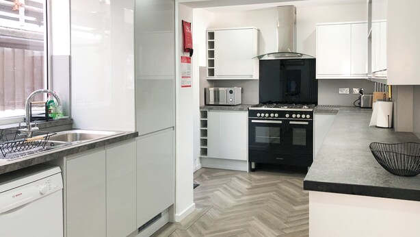 Une cuisine moderne avec des meubles blancs, un lave-vaisselle Bosch, une cuisinière noire et un plancher à motifs en chevrons.