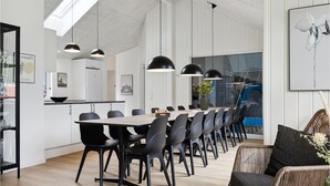 Un comedor moderno con una mesa larga y sillas, iluminación colgante, y vistas a la cocina y el comedor.