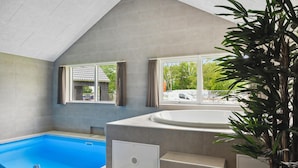 Una piscina interior moderna con un jacuzzi, ventanas amplias y una escalera.
