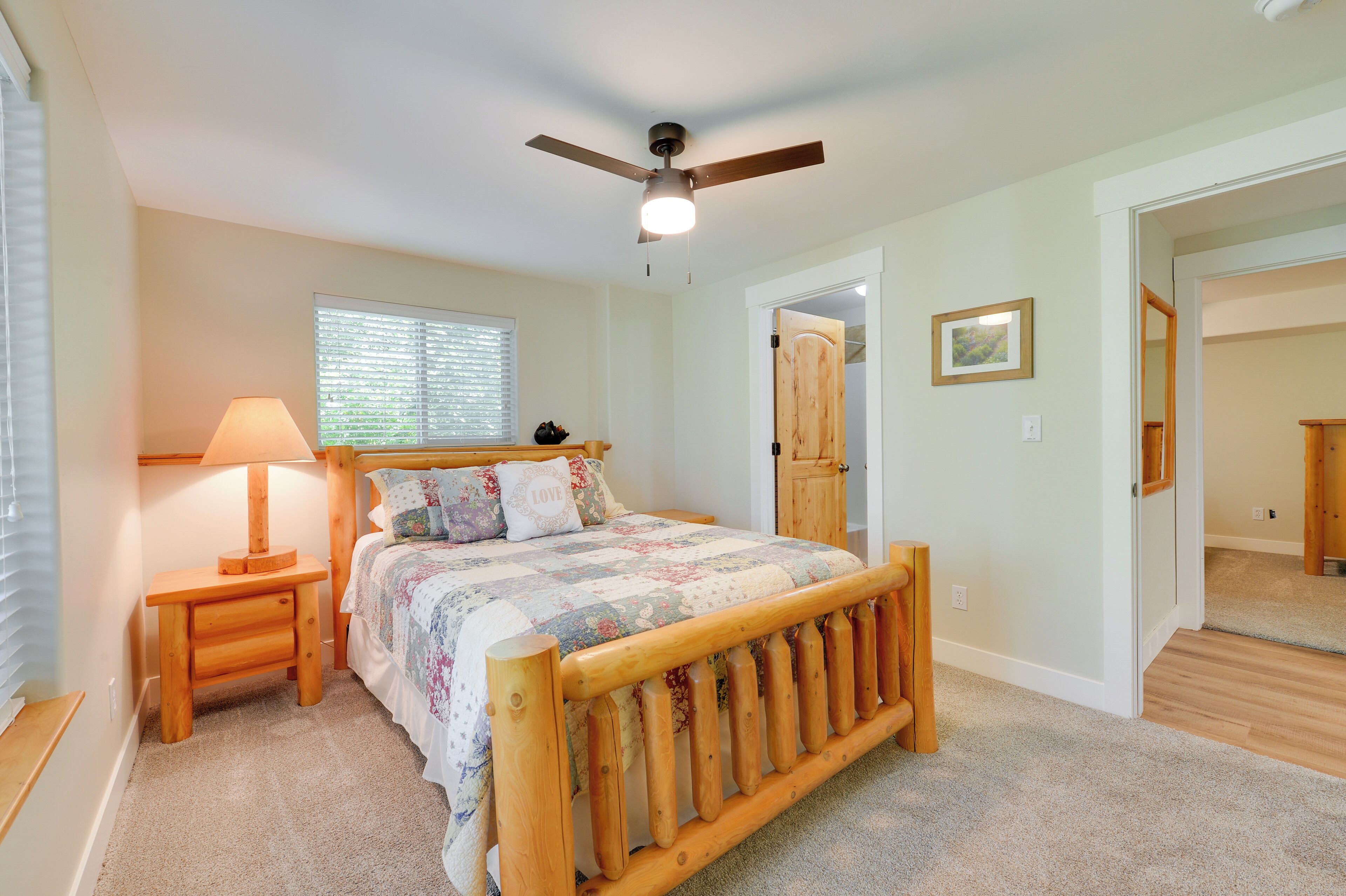 A bedroom with a wooden bed, a ceiling fan, a bedside table with a lamp, and a window with blinds.