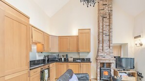Ein gemütlicher, kompakter Wohnraum mit Küchenzeile, Kamin, Fernseher und Ledersofa.