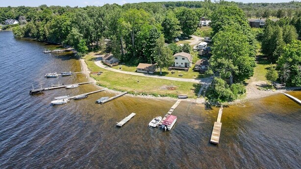 An aerial view of a lakeside property with docked boats, a house surrounded by trees, and a clear sky. - LAKEFRONT COTTAGE #5 - PRINCE EDWARD COUNTY - LAKE CONSECON RESORT (Prince Edward)
