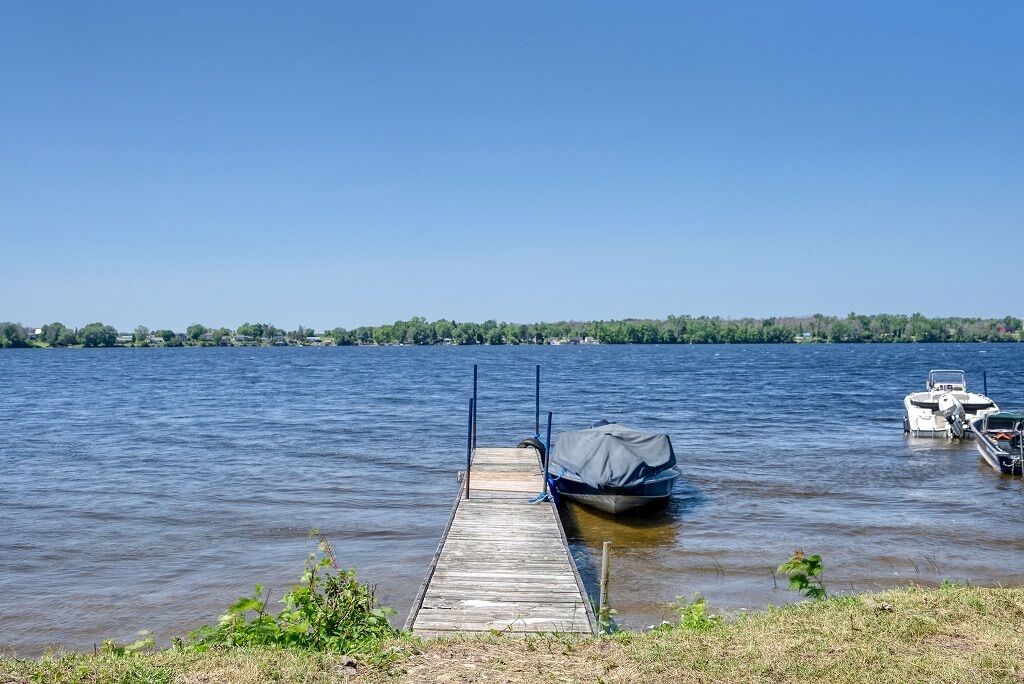 A wooden dock extending into calm water with a covered boat and another boat docked nearby.