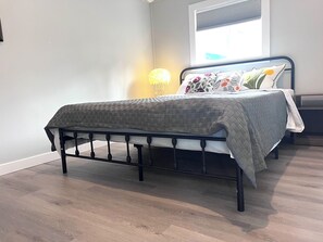Un dormitorio con cama, ventana con persianas y lámpara.
