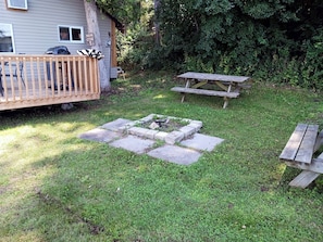 Un patio trasero con terraza de madera, una mesa de picnic y un área con fogata.