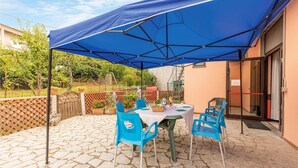 Un patio con mesa y sillas bajo un paraguas azul, rodeado de un suelo de baldosas de piedra y una valla de madera.