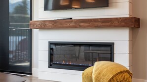 A modern living room with a flat-screen TV mounted above a fireplace, a yellow ottoman, and a striped rug. - Northern Exposure by Revelstoke Vacations (Revelstoke)