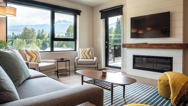 A modern living room with a sofa, armchairs, a coffee table, a fireplace, and a large TV. - Northern Exposure by Revelstoke Vacations (Revelstoke)