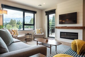 A modern living room with a sofa, armchairs, a coffee table, a fireplace, and a large TV. - Northern Exposure by Revelstoke Vacations (Revelstoke)