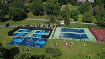 An aerial view of a sports complex with multiple tennis courts, surrounded by trees and residential buildings.