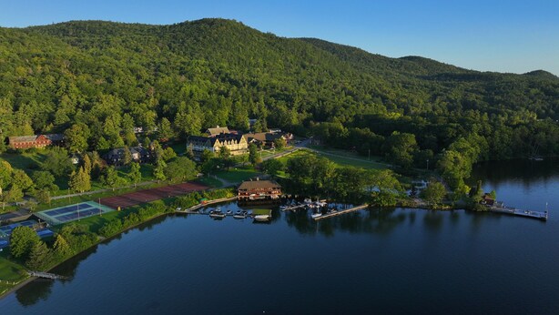 A lakeside property with a tennis court, dock, and multiple buildings surrounded by forested hills.
