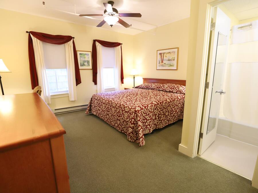 A bedroom with a bed, a ceiling fan, a door, and a window with curtains.