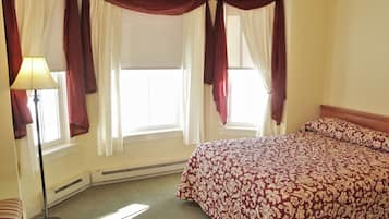A hotel room with a bed, a floor lamp, and windows with curtains.