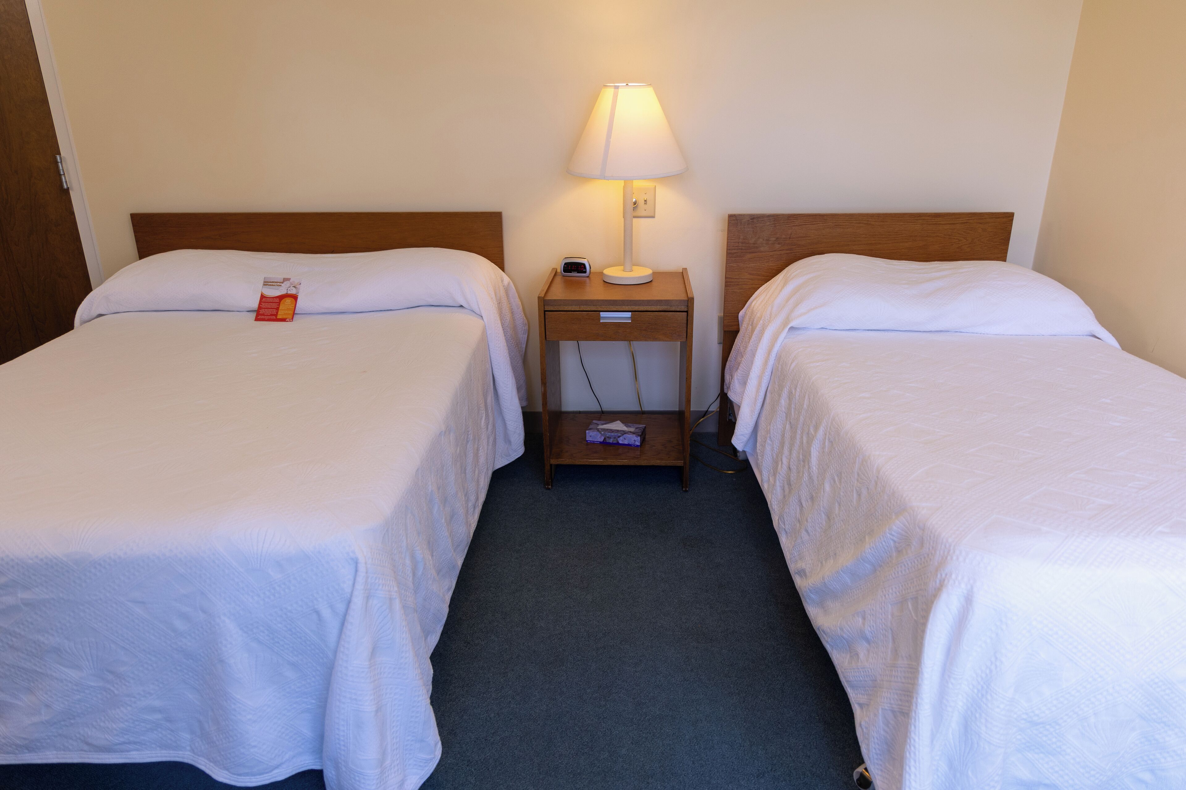 Une chambre d’hôtel avec deux lits simples, une table de chevet avec une lampe et un petit tiroir.