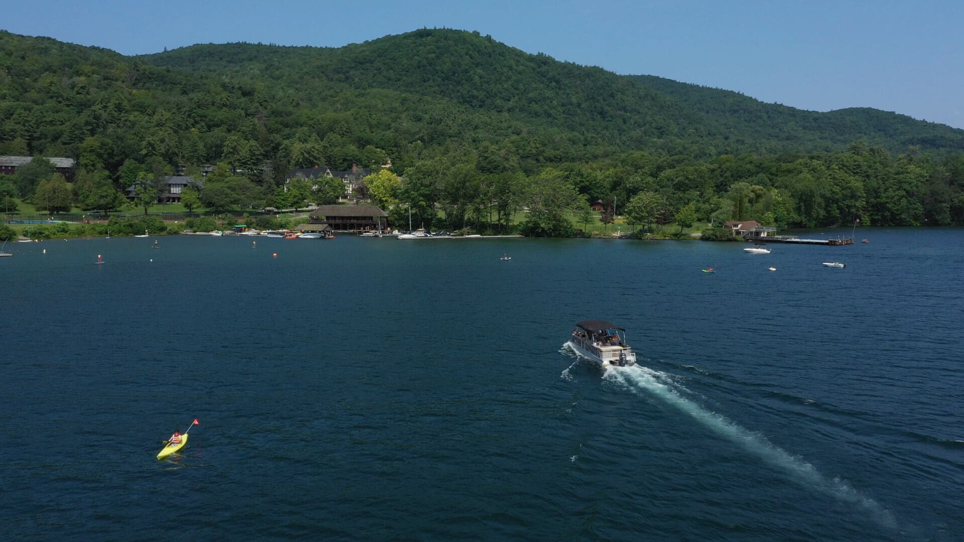A lake with a boat in motion, surrounded by houses and a forested hill.