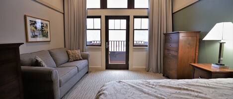 A hotel room with a bed, a sofa, a dresser, and a window with curtains.