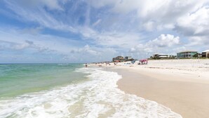 A beach with clear waters, a sandy shore, and buildings in the background.