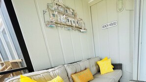 A cozy living area with a grey sofa, yellow and orange patterned cushions, a wicker side table, and a sign reading "BEACH HOUSE".