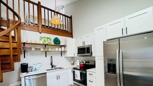 A modern kitchen with white cabinets, a stainless steel refrigerator, a microwave, and a coffee machine.